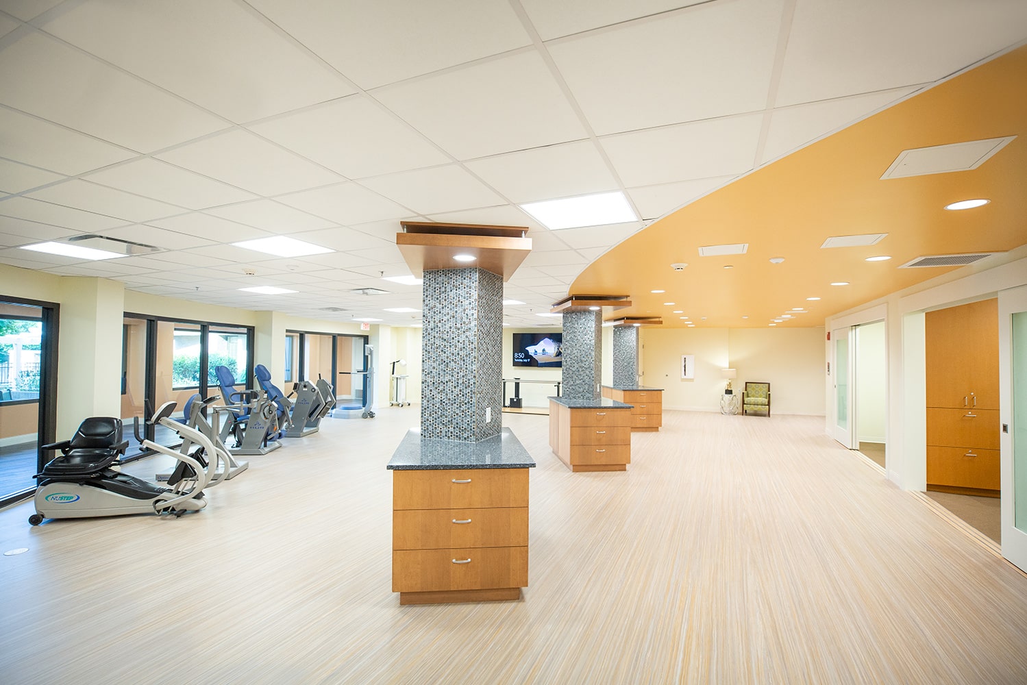 Bright and clean fitness facility with machines along the left wall and a large tv in the background