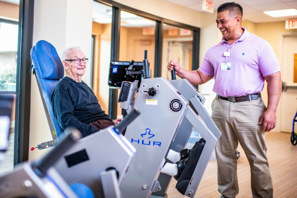 Trainer helping elderly man on fitness machine in the gym
