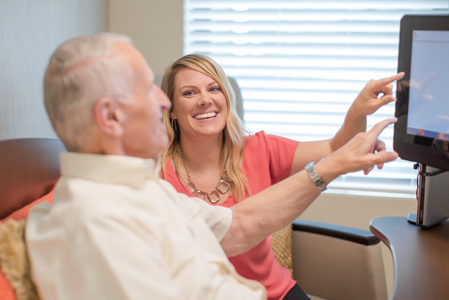 Woman smiling at older man and pointing to computer screen