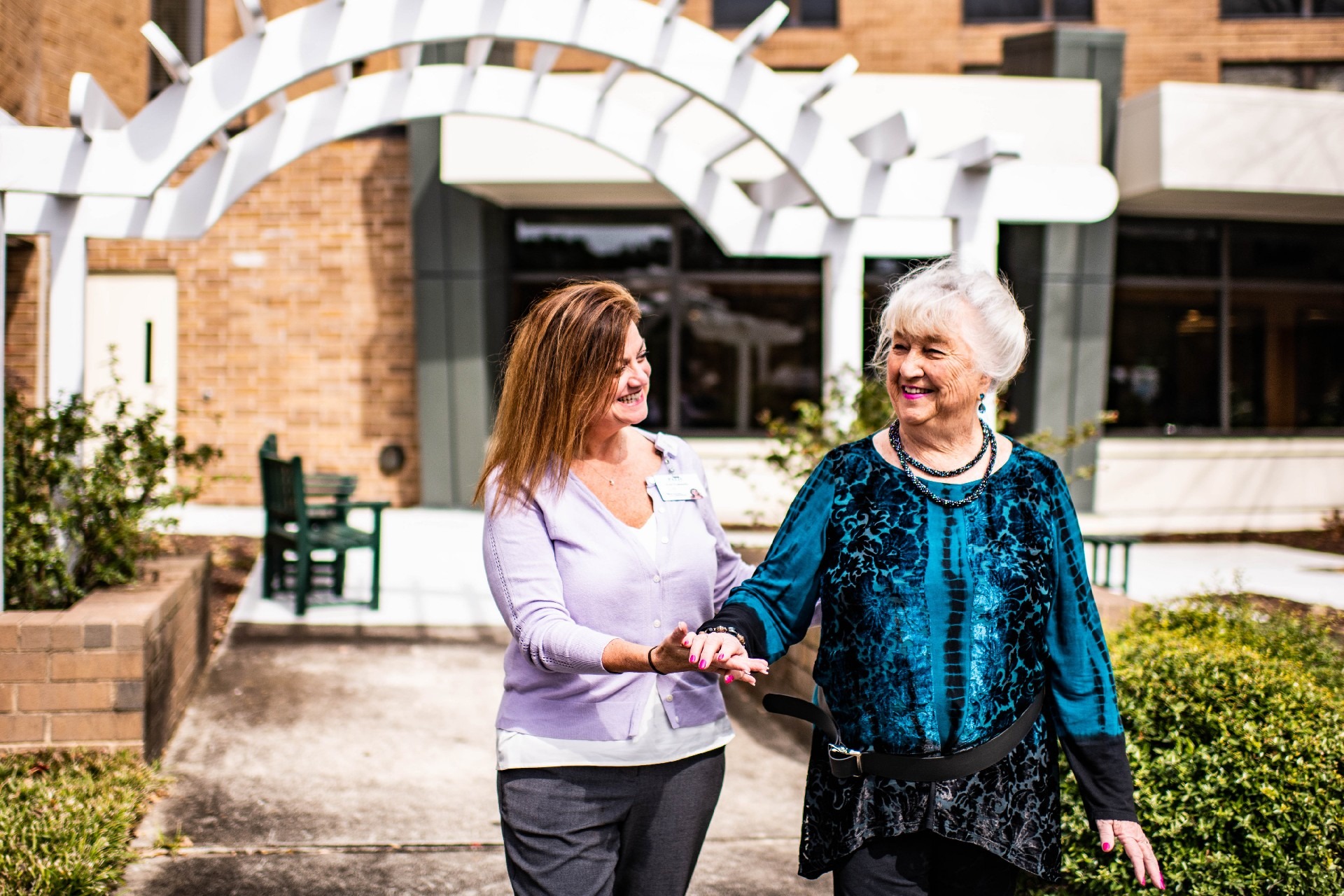 Woman smiling and guiding elderly woman on a walk outside