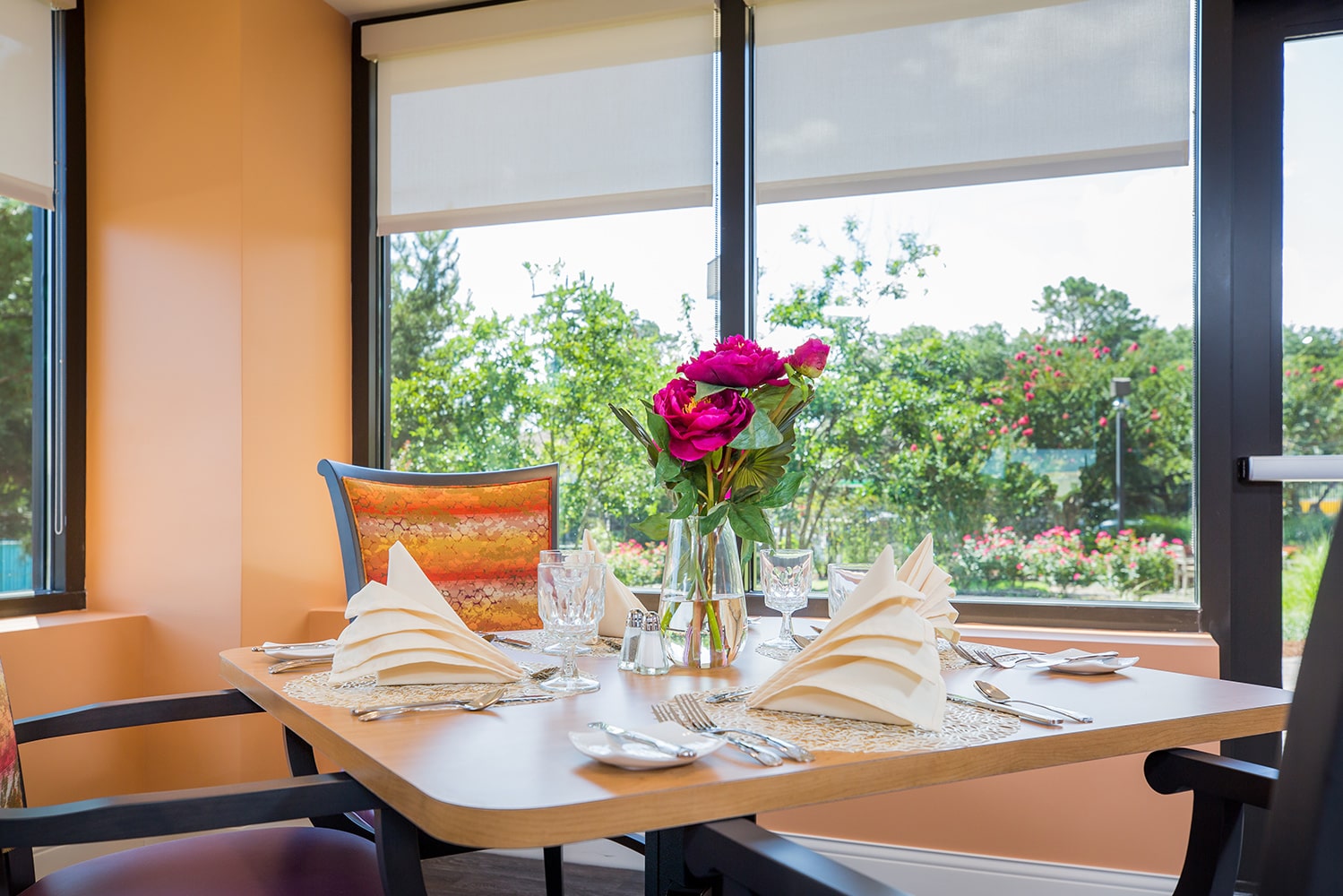 Dinner table set with crystal glasses, plates, and cloth napkins with a vase of roses in the center of the table