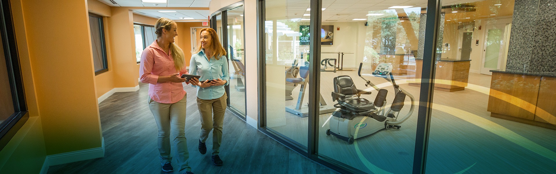 Two women walking down the hallway outside the gym facility talking to each other