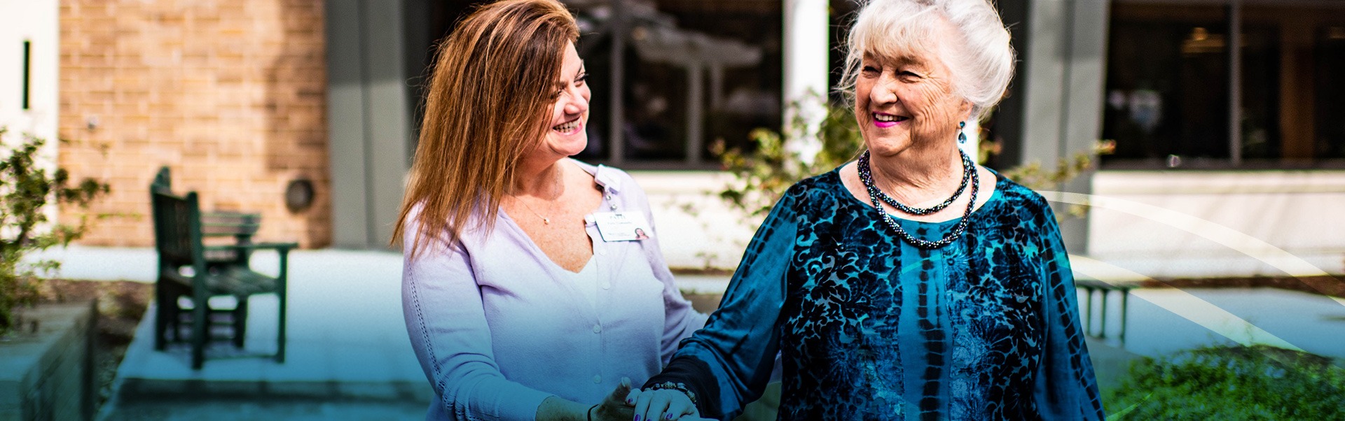 Woman smiling and guiding elderly woman on a walk outside